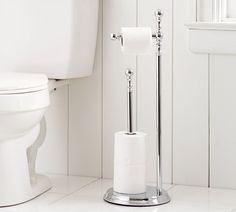 a white toilet in a bathroom next to a roll of toilet paper and a metal holder