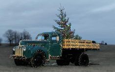 an old green truck with a christmas tree on the back is parked in a field