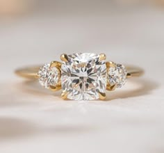 a three stone diamond ring on a white surface with gold trim around the band and sidestones