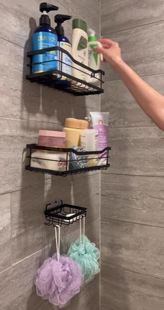 a person is holding soap and shampoo in front of a shower wall with three shelves