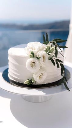 a white wedding cake with flowers on top is sitting on a table near the ocean