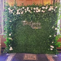 a green wall with white flowers and greenery at the entrance to a wedding ceremony