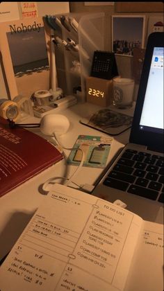 a laptop computer sitting on top of a desk next to a book and other items