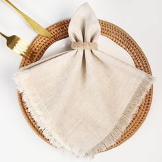 a place setting with two forks and a napkin on a wicker plate topped with a gold fork