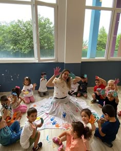 a group of children sitting on the floor in front of a woman with her hands up