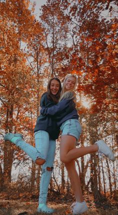 two young women are posing for the camera in front of trees with orange leaves on them