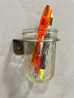 there is a glass jar with some pens in it and a hook on the wall