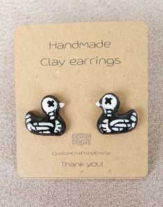 a pair of black and white ducky earrings on top of a cardboard card that says handmade clay earrings