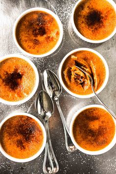 four bowls of soup with spoons and silverware on a metal surface, ready to be eaten