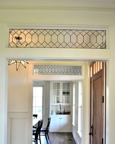 an open door leading to a kitchen and dining room area with white walls, wood flooring and stained glass windows