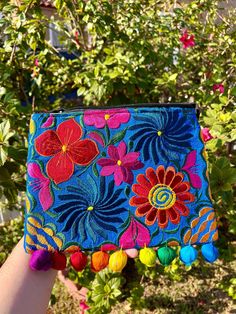 a hand holding up a colorful embroidered pouch