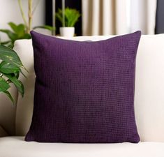 a purple pillow sitting on top of a white couch next to a potted plant