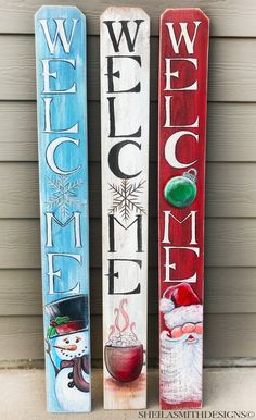 three painted wooden signs sitting on the side of a building with snowmen and sleds