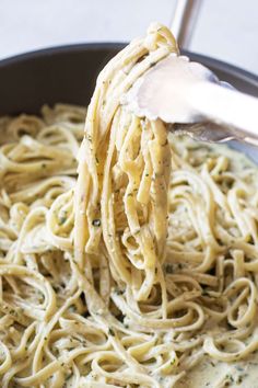 a ladle full of pasta being held up by a metal spoon in a skillet