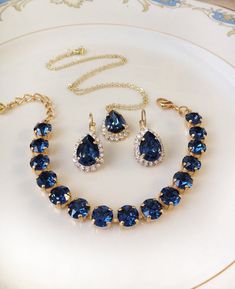 "Gorgeous bracelet, earrings and necklace set. Bracelet featuring 8mm round Swarovski crystals in rich navy blue. The bracelet is adjustable between 6 1/2 and 8 1/2\". Earrings: 14x10mm navy blue teardrop shaped crystals in clear crystal halo settings. Lever back earring closure for pierced ears. Necklace: 14x10mm Navy blue teardrop shaped crystal in a clear crystal halo setting, chain and clasp. Love this rich navy blue! Available in gold plated settings, as shown, rose gold or silver plated. P Gold And Navy Jewelry, Navy Blue Jewelry Set, Gold And Sapphire Necklace, Adjustable Sapphire Crystal Jewelry, Elegant Adjustable Blue Jewelry Sets, Elegant Adjustable Sapphire Jewelry, Adjustable Crystal Jewelry For Bridesmaid Gift, Blue And Gold Jewelry, Sapphire Jewelry Set