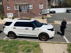 a man standing next to a white car in a parking lot near a brick building