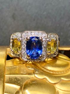 A colorful 3 stone ring done in 18K white gold centered by an approximately 2.32ct oval cut natural blue sapphire (heat only) flanked by two yellow sapphires totaling 1cttw. Surrounding the sapphires is approximately .52cttw in H-I color Vs2-Si1 clarity round diamonds. Dimensions/Weight: Ring measures .50" top to bottom and .65" wide and weighs 10g. Sz 7 (sizable). Condition: All stones are secure and in perfectly wearable condition. R-CVVG Luxury Multi-stone Classic Sapphire Ring, Luxury Yellow Gold Sapphire Ring With Gemstone Accents, Luxury Unique Multi-stone Sapphire Ring, Yellow Multi-stone Sapphire Ring, Multicolor Oval Sapphire Ring, Oval Multi-stone Sapphire Gemstones, Blue Sapphire Ring With Three Stones, Oval Blue Multi-stone Sapphire Ring, Luxury Yellow Oval Sapphire Ring