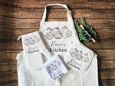 three kitchen aprons with embroidered designs on them sitting on a wooden table next to some scissors