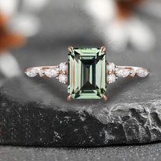 an emerald and diamond ring sitting on top of a black stone slab with diamonds around it