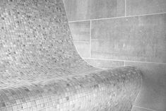 a black and white photo of a bench in front of a wall with mosaic tiles on it