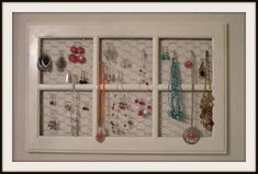 a wall mounted jewelry organizer in a white frame with six glass panes filled with earrings