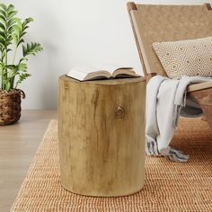 an open book is sitting on top of a wooden table next to a chair and potted plant