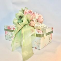 a gift box with flowers on it and a green ribbon tied around the top, sitting on a white surface