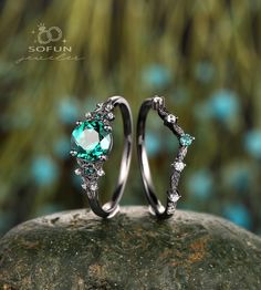 two wedding rings with green and white stones on top of a rock in front of some trees