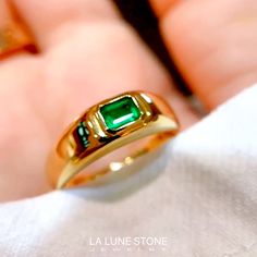 a close up of a person's hand holding a gold ring with a green stone