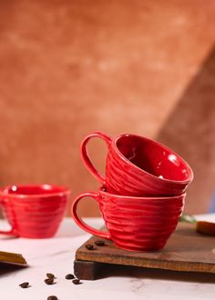 three red cups sitting on top of a wooden board next to coffee beans and a book