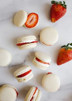 macaroons and strawberries are arranged on a marble surface