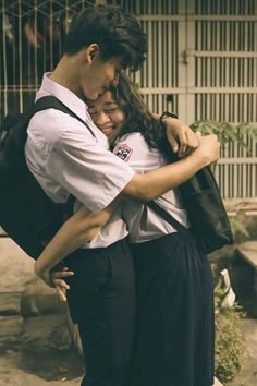 two people hugging each other in front of a fence