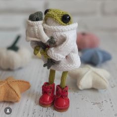 a small toy frog wearing red boots and a white sweater