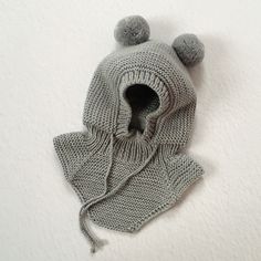 a gray knitted hat with two pompons on the top and one ear