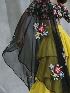 This vibrant set features a black off shoulder blouse in silk and net base with cutdana and multi-coloured thread hand embroidered floral motifs. It is paired with a yellow ruffles tiered lehenga skirt and a black net dupatta. Spring Party Sets With Multicolor Embroidery, Yellow Sharara With Floral Embroidery For Party, Yellow Floral Embroidery Sharara For Party, Yellow Floral Embroidered Sharara For Party, Traditional Yellow Ruffled Sharara, Spring Festive Lehenga With Sheer Dupatta, Festive Spring Lehenga With Sheer Dupatta, Floral Embroidery Sharara For Summer Parties, Yellow Organza Blouse Piece For Party