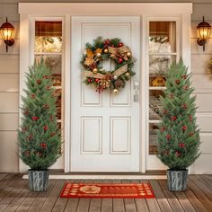 two christmas wreaths are on the front door of a house with potted trees