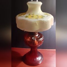 an old fashioned lamp is sitting on a red tableclothed surface, with yellow flowers painted on it