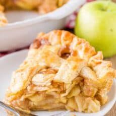 a slice of apple pie on a white plate with a fork next to the pie