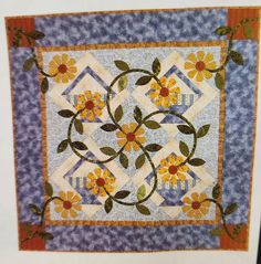 a quilted wall hanging with flowers and leaves on the front, along with an orange border