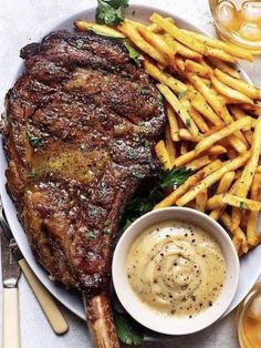 a plate with steak, fries and sauce on it next to some glasses of beer