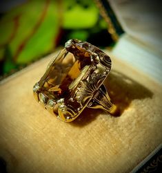 A gleaming golden emerald-cut citrine is presented in a fancifully filigreed mounting, adorned with beautiful waves and leaves. Details Gemstone: Citrine Carat Total Weight: 5 ct. Color: Yellow Metal Type : 585 Yellow Gold Hallmark: 14K Total Weight: 7 gr. Measurements: 20,0 mm x 15,5 mm Size: EU 57 All measurements were done in the mounting as allowed by an independent, GIA-trained gemologist and are approximate when noted. Some of our items are accompanied by a lab report, but not all. It will Luxury Citrine Topaz Ring With Emerald Cut, Elegant Emerald Cut Topaz Ring With 17 Jewels, Formal Yellow Gold Topaz Ring With Rectangular Stone, Elegant Emerald Cut Topaz Ring, Antique Emerald Cut Diamond Jewelry, Art Deco Emerald Cut Topaz Ring, Luxury Rectangular Topaz Ring For Formal Occasions, Victorian Emerald Cut Jewelry For Formal Occasions, Victorian Emerald Cut Formal Jewelry