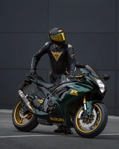 a man in black and yellow is standing next to a green motorcycle with gold accents