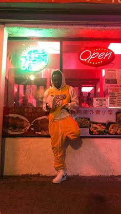 a person in an orange outfit sitting on a ledge outside of a food stand at night