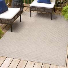 two wicker chairs sitting on top of a wooden deck next to a white rug