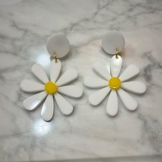 two white and yellow flower shaped earrings on a marble surface