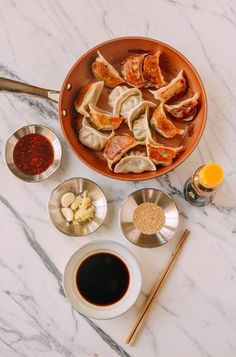 a bowl filled with dumplings next to bowls of sauces and chopsticks