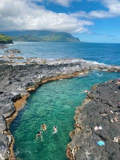 two people swimming in the ocean next to some rocks and water with an island in the background