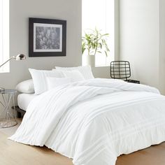 a bed with white comforter and pillows in a room next to a lamp on a table