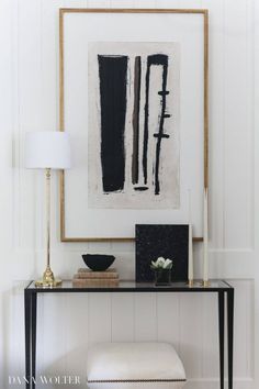 a black and white painting hangs on the wall above a console table with a lamp