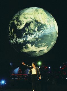 a man standing on top of a stage in front of a large screen with the earth